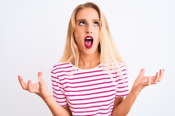 Young beautiful woman wearing pink striped t-shirt standing over isolated white background crazy and mad shouting and yelling with aggressive expression and arms raised. Frustration concept.