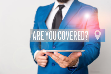 Writing note showing Are You Covered Question. Business concept for asking someone or patient if he have insurance Businessman in blue suite with a tie holds lap top in hands