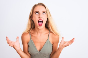 Young beautiful woman wearing casual green t-shirt standing over isolated white background crazy and mad shouting and yelling with aggressive expression and arms raised. Frustration concept.