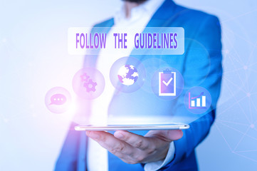 Conceptual hand writing showing Follow The Guidelines. Concept meaning Manual of Style Follow a Specified Rule Accordingly Male human wear formal suit presenting using smart device
