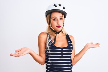 Young beautiful woman wearing bike helmet standing over isolated white background clueless and...