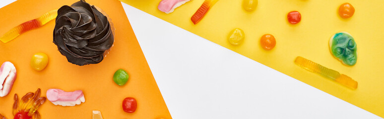 panoramic shot of gummy sweets and cupcakes on yellow and white background, Halloween treat