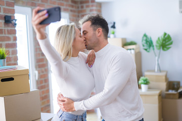 Young beautiful couple standing using smartphone to take selfie kissing at new home around cardboard boxes