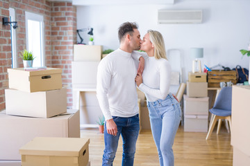 Fototapeta na wymiar Young beautiful couple standing kissing at new home around cardboard boxes