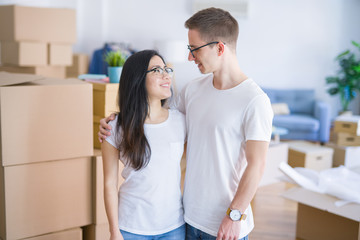 Fototapeta premium Young beautiful couple wearing glasses standing at new home around cardboard boxes