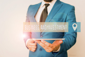 Writing note showing Business And Investment. Business concept for putting your money in field to increase them Businessman in blue suite with a tie holds lap top in hands