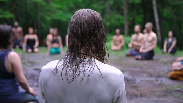 Diverse people enjoy spiritual gathering A close up and rear view of a person with soaked hair and t-shirt during a group meditation session in a forest clearing at a shamanic celebration in nature.