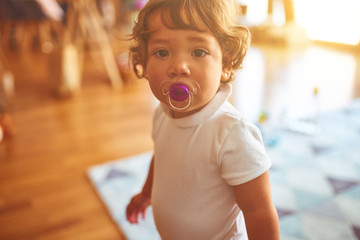 Beautiful toddler child girl wearing white t-shirt standing on the floor using pacifier