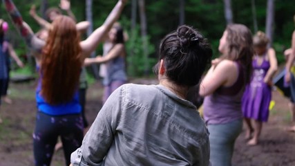 Diverse people enjoy spiritual gathering A young woman wearing grey shirt with short black hair is seen from the rear, experiencing free shamanic dance used to balance chakra and reach tranquility.
