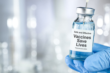 Healthcare concept with a hand in blue medical gloves holding a vaccine vial wtih the words Safe and Effective, Vaccines Save Lives, and does not cause autism - obrazy, fototapety, plakaty