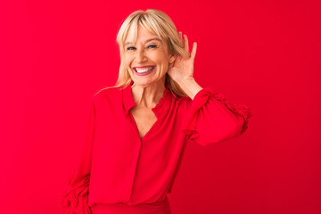 Middle age woman wearing elegant shirt standing over isolated red background smiling with hand over...