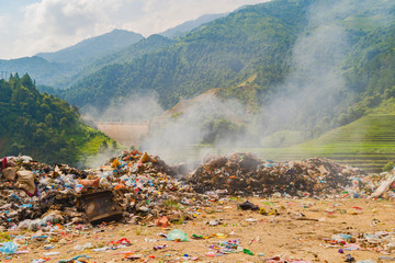 Stack of different types of large garbage dump, plastic bags, and trash burning near paddy rice...