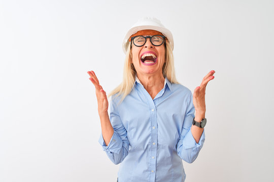 Middle age architect woman wearing glasses and helmet over isolated white background celebrating mad and crazy for success with arms raised and closed eyes screaming excited. Winner concept
