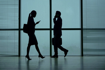 Silhouettes of business people walking in airport terminal, talking on phone and texting