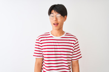 Young chinese man wearing glasses and striped t-shirt standing over isolated white background winking looking at the camera with sexy expression, cheerful and happy face.
