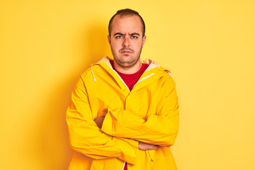 Young man wearing rain coat standing over isolated yellow background skeptic and nervous,...