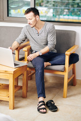 Handsome young man wearing wireless earbuds when checking e-mails on laptop