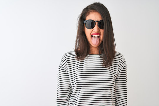 Chinese woman wearing striped t-shirt and sunglasses standing over isolated white background sticking tongue out happy with funny expression. Emotion concept.