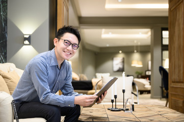 Asian man real estate agent hands holding clipboard document sitting on sofa in example house