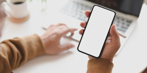 Young man working on his project while typing on laptop computer and holding smartphone