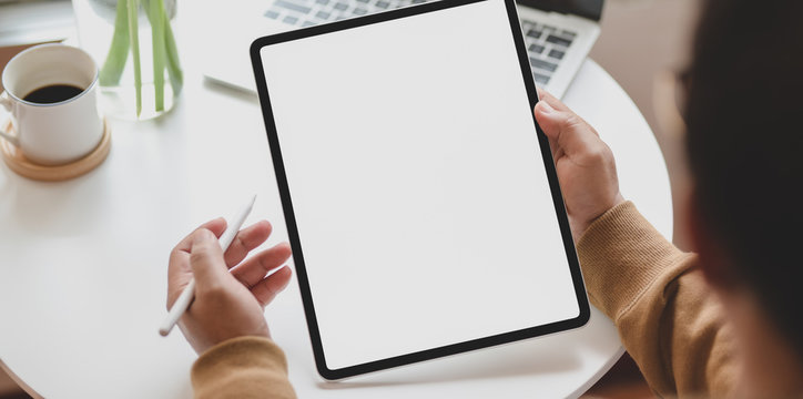 Close-up view of young man holding blank screen vertical tablet in his workspace