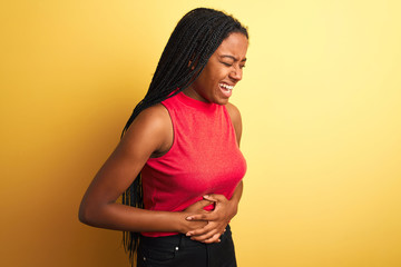 African american woman wearing red casual t-shirt standing over isolated yellow background with hand on stomach because indigestion, painful illness feeling unwell. Ache concept.