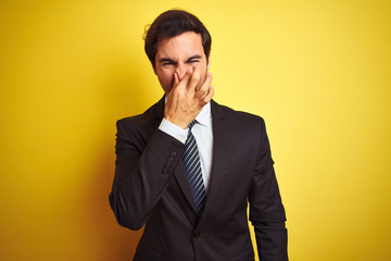 Young handsome businessman wearing suit and tie standing over isolated yellow background smelling...
