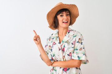 Beautiful woman on vacation wearing summer shirt and hat over isolated white background with a big smile on face, pointing with hand and finger to the side looking at the camera.