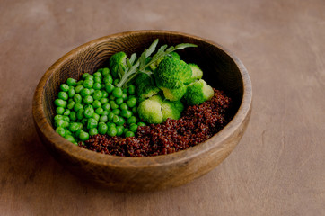 Healthy and teasty greeen bowl with red quinoa, peas, broccoli in textured wooden plate, with place for text.