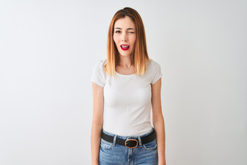 Beautiful redhead woman wearing casual t-shirt standing over isolated white background winking looking at the camera with sexy expression, cheerful and happy face.