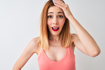 Beautiful redhead woman wearing casual pink t-shirt standing over isolated white background stressed with hand on head, shocked with shame and surprise face, angry and frustrated. Fear 