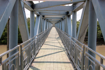 A empty metal foot bridge, perspective view. Construction of iron bridge over water. Pedestrian transition over the river.