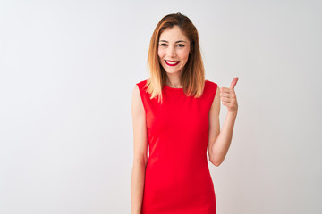 Redhead businesswoman wearing elegant red dress standing over isolated white background doing happy thumbs up gesture with hand. Approving expression looking at the camera showing success.