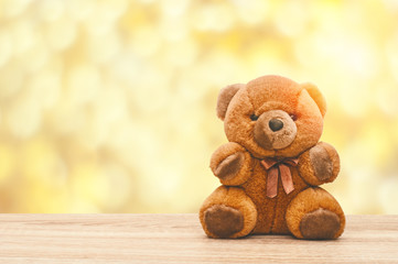 Toy brown bear is sitting on a wooden table on blurred sunny background.