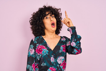Young arab woman with curly hair wearing floral dress over isolated pink background pointing finger up with successful idea. Exited and happy. Number one.