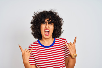 Young arab woman with curly hair wearing striped t-shirt over isolated white background shouting with crazy expression doing rock symbol with hands up. Music star. Heavy concept.