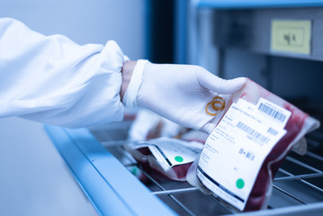 Selective focus scientist hand holding red blood bag in storage blood refrigerator at blood bank unit laboratory in the hospital.Save life and medical treatment concept. - obrazy, fototapety, plakaty