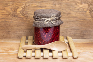 jar with raspberry jam stands on a wooden background