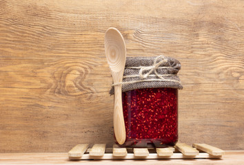 jar with raspberry jam stands on a wooden background