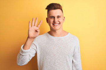 Young handsome man wearing white casual t-shirt standing over isolated yellow background showing and pointing up with fingers number four while smiling confident and happy.