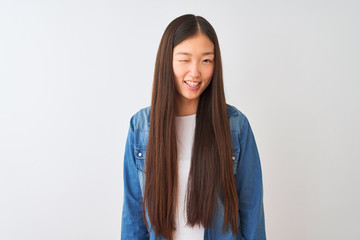 Young chinese woman wearing denim shirt standing over isolated white background winking looking at...