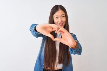 Naklejka premium Young chinese woman wearing denim shirt standing over isolated white background smiling in love doing heart symbol shape with hands. Romantic concept.