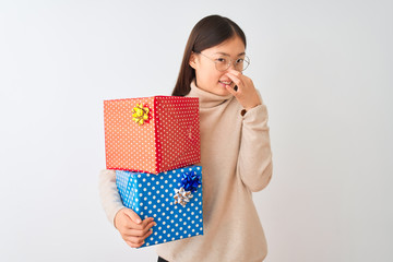 Young chinese woman holding birthday gifts over isolated white background smelling something stinky and disgusting, intolerable smell, holding breath with fingers on nose. Bad smells concept.