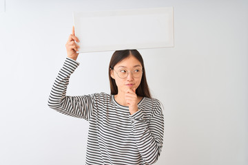 Young chinese woman wearing glasses holding banner over isolated white background serious face...