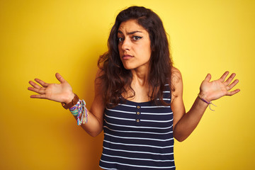 Young beautiful woman wearing striped t-shirt standing over isolated yellow background clueless and...