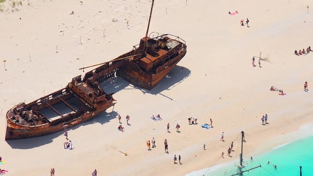 People relaxing and sunbathing on Navagio Beach or Shipwreck Beach. Old ship after crash lying on sand. Tourists swimming on turquoise Ionian Sea. Paradise in lagoon of Zakynthos island, Greece