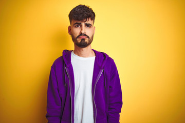 Young man with tattoo wearing sport purple sweatshirt over isolated yellow background depressed and worry for distress, crying angry and afraid. Sad expression.