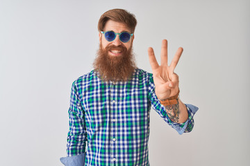 Young redhead irish man wearing casual shirt and sunglasses over isolated white background showing and pointing up with fingers number three while smiling confident and happy.