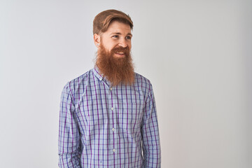 Young redhead irish man wearing casual shirt standing over isolated white background looking away to side with smile on face, natural expression. Laughing confident.