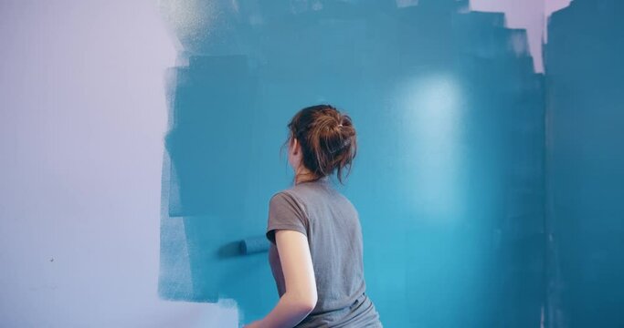 Teenage girl painting room wall with paint roller in 4K slow motion